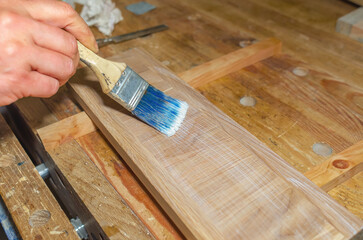 carpenter applies glue to surface of board with brush in carpentry workshop