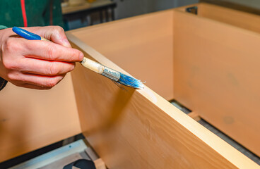 carpenter applies glue to surface of board with brush in carpentry workshop