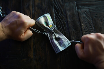 Hands Chained Together Holding Crumpled American Dollar Bills on Dark Wooden Surface