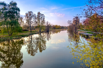 Tranquil river scene with trees reflected in water at sunset.