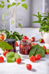 Homemade strawberry jam surrounded by fresh strawberries and leaves
