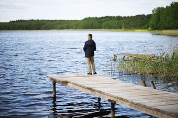 Boy Fishing Alone on a Wooden Dock by a Peaceful Lake During Daytime