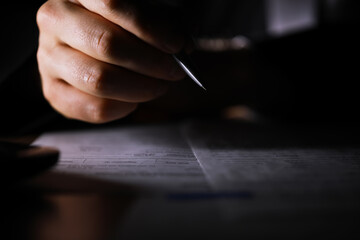 Close-Up Pen In Hand Signing Document In Low Light Setting - Business And Legal Concept