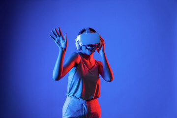 Smart female standing surrounded by neon light wearing VR headset connecting metaverse, future...
