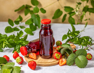 Two bottles of strawberry juice surrounded by fresh strawberries and mint leaves