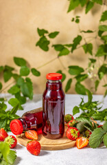 Two bottles of fresh strawberry juice surrounded by ripe strawberries and green leaves