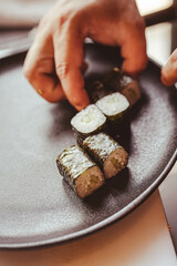 A chef carefully places freshly prepared sushi rolls on a plate by hand. Perfect for illustrating traditional sushi preparation and serving techniques in fine dining settings.