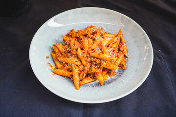 Side view of a plate of penne pasta with rich Bolognese sauce served on a plain grey plate. Perfect for Italian food menus, restaurant promotions, or pasta lovers.
