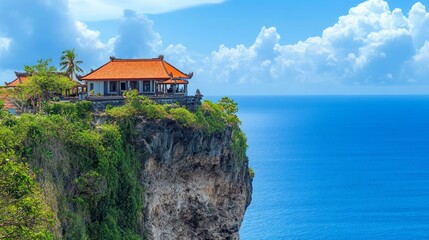Obraz premium A traditional Asian temple perched on a cliff overlooking a vast blue ocean with white clouds in the sky.
