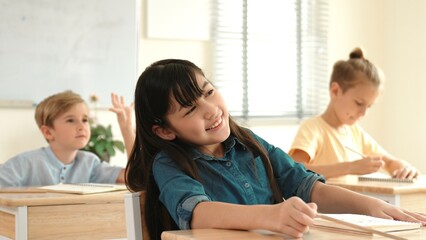 Smart elementary student looking at teacher while attend in classroom. Diverse smart student sitting at classroom while listening teacher explain about classwork or test. Education concept. Pedagogy.