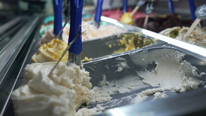 Close-up of a gelato display at an ice cream shop, showcasing various flavors with metal scoops ready for serving. A tempting and colorful scene capturing the allure of sweet treats