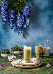 Iced matcha latte decorated with flower standing on table with green tiles