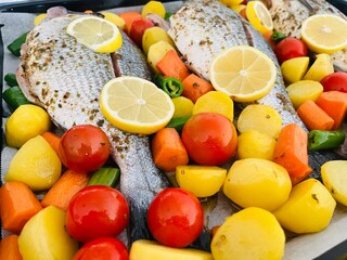 Fish on a baking tray decorated with potatoes, tomatoes and green peppers