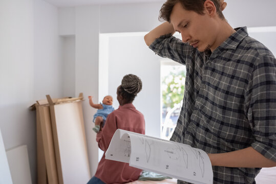 Father reading manual near wife with baby at home