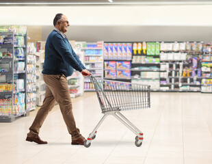 Full length profile shot of a mature man walking and pushing an empty shopping cart