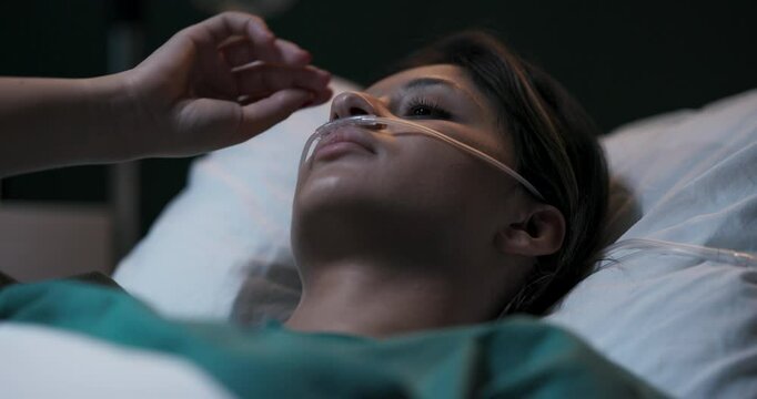 Young woman lying in hospital bed with oxygen tube in her nose.