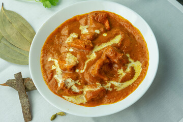 A steaming bowl of rich, creamy tomato curry features tender chunks of meat, drizzled with fresh cream. Surround the dish with colorful garnishes like cilantro and vibrant spices.