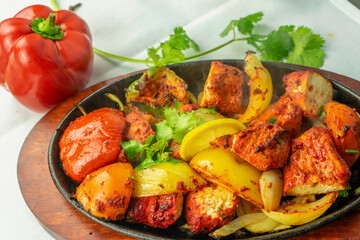 Sizzling platter of grilled vegetables and spices. with bell peppers in red, yellow, and green, alongside juicy tomatoes and marinated grilled meat or paneer, garnished with fresh cilantro.