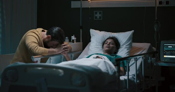 Young girl lies unconscious in a hospital bed with an oxygen tube in her nose. Beside her sits a tired-looking man.