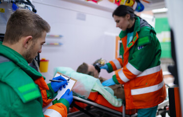 Paramedics in green and orange uniforms provide care to male patient on stretcher inside an...