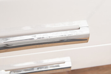 White plaque from hard water on handles of the bathroom cabinet. Silver chrome handle