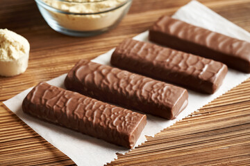 Healthy vegetarian protein chocolate bars with a bowl of whey protein powder on a table