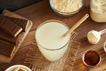 Fresh whey protein drink in a glass cup with a bamboo straw with whey protein bars and powder