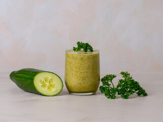 cucumber and parsley juice the best detox for the body, a glass of green juice next to a green cucumber and a sprig of green parsley