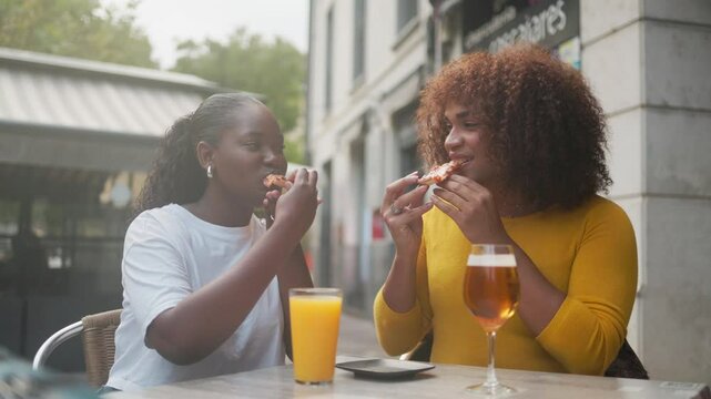 Two women friends eating a slice of pizza and sharing the experience. Gen z lifestyle.