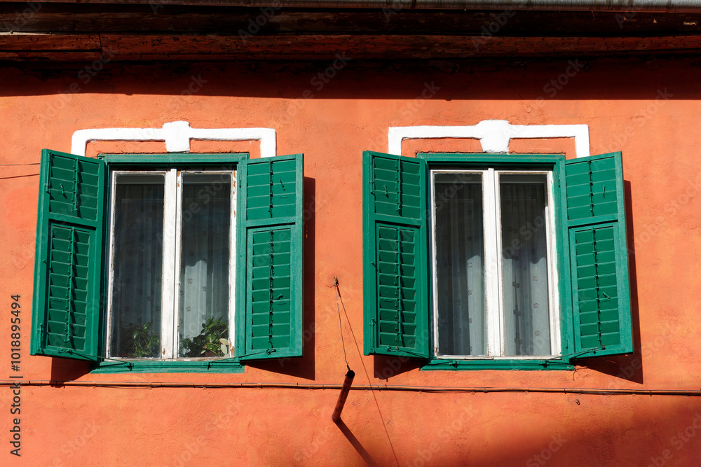 Wall mural two green wooden shutters partially open on a bright orange wall. the windows behind the shutters ha