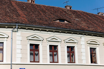 A close-up view of a traditional building facade in Sibiu, Romania, featuring a red tiled roof with a distinctive arched shape. The building also has several window with white trim and brown frames.