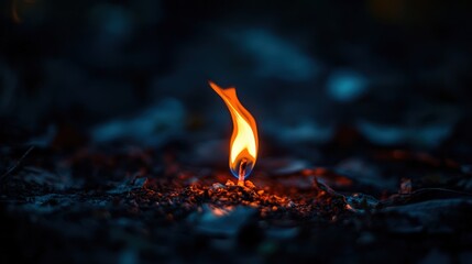 A small flame ignites in a dark setting, radiating warmth and energy amidst shadows, creating a captivating visual