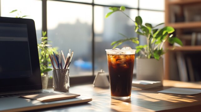 Iced coffee on a desk with laptop, plants and pencils.