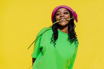 African smiling woman with flower in mouth at vibrant yellow backdrop