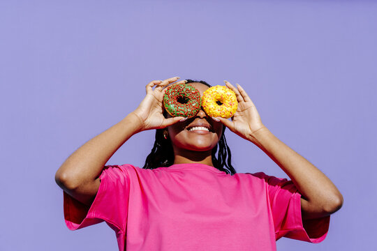 Smiling woman holding colorful donuts over her eyes