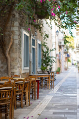 Fototapeta premium In the heart of Nafplio, Greece, rustic wooden tables sit quietly under the shade of lush leaves, creating a perfect setting for relaxed meals and warm conversations.