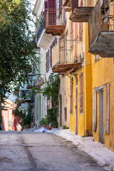 Wander down a narrow street in Nafplio, Greece, where brightly painted traditional houses stand adorned with balconies, showing off the town's unique charm and inviting atmosphere.