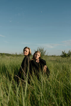 Mother and a daughter in Dark Outfits Sitting in the tall green grass