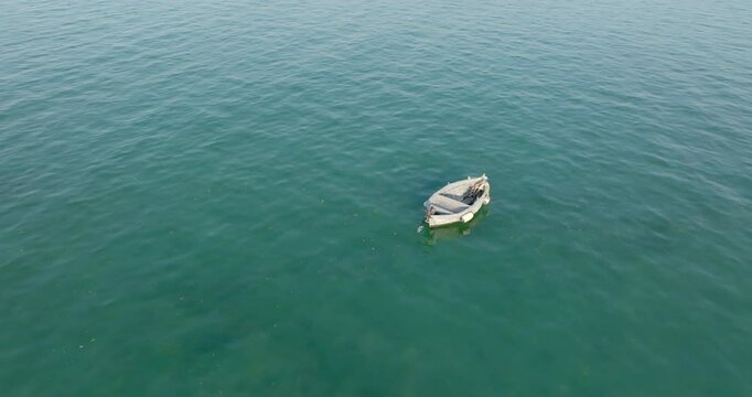 Aerial view of a one small fishing boat anchored in the middle of the sea. The boat is empty and lonely.