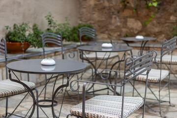 A serene courtyard invites relaxation with several elegant tables and stylish chairs, accented by lush greenery, creating a perfect spot for enjoying drinks in the sunshine.
