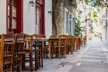 Quaint wooden tables set under blooming flowers create a welcoming ambiance along the narrow streets of Nafplio, showcasing the city's charming character.