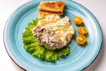 Scrambled eggs with mushrooms and crispy toast garnished with lettuce and yellow cherry tomatoes, on a turquoise plate, on a white table. Delicious and healthy breakfast