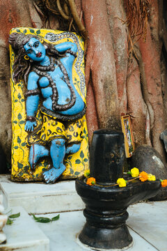 Blue deity statue adorned with flowers near stone shrine in temple