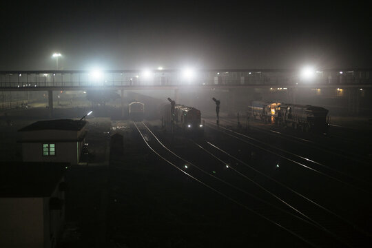 Nighttime view of a railway station with fog and illuminated tracks