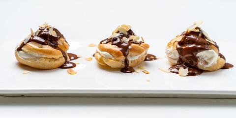 Profiteroles according to a traditional French recipe with custard, drizzled with chocolate and decorated with almond petals on a white background