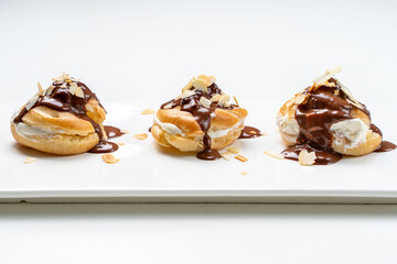 Profiteroles according to a traditional French recipe with custard, drizzled with chocolate and decorated with almond petals on a white background
