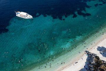 Drone Aerial view of tourists enjoying summer on a Greek isolated tropical beach with turquoise water.