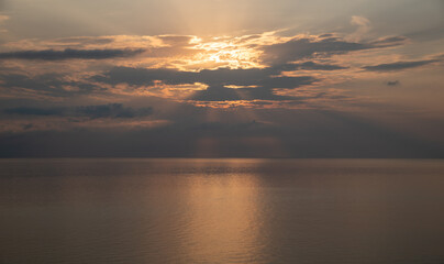 Obraz premium Sun shining through clouds over calm ocean at sunrise