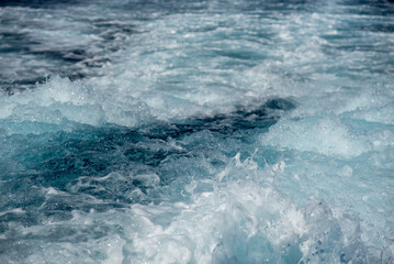 Turquoise blue ocean water foaming behind a ship