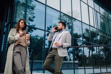 Business people using smartphones and drinking coffee outside office building